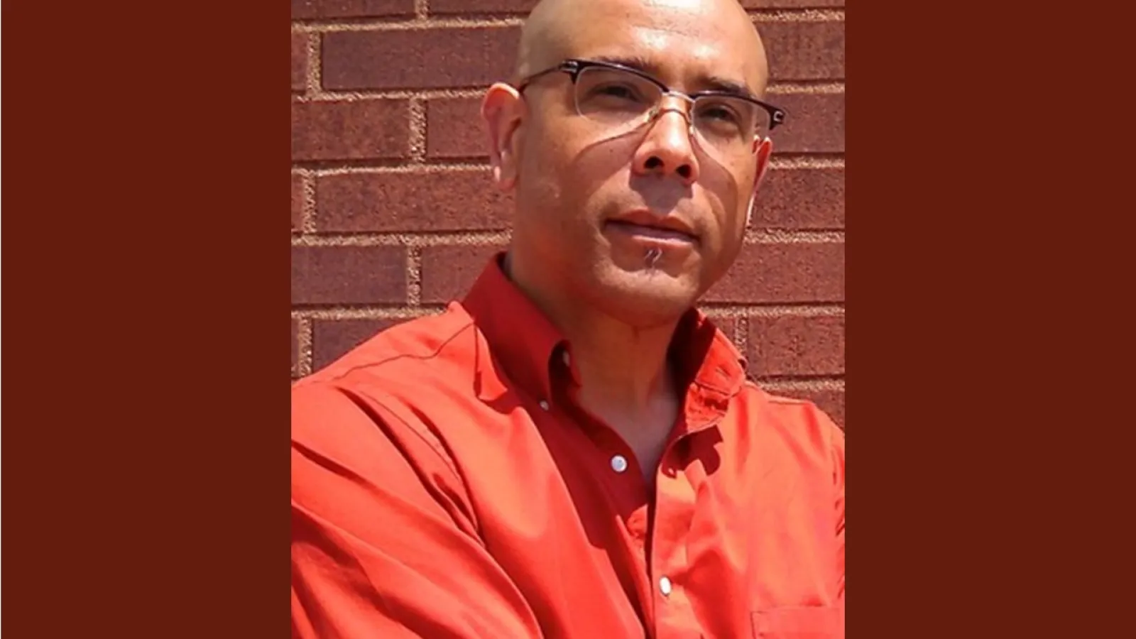 Individual wearing glasses and reddish orange shirt