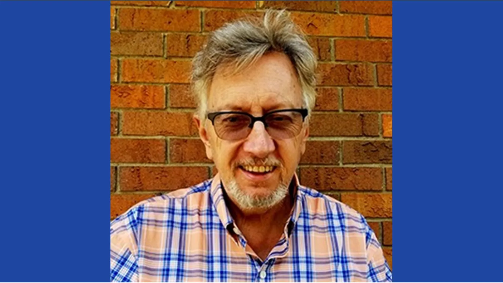 Dr. John Low wearing glasses, with a light orange and blue shirt.