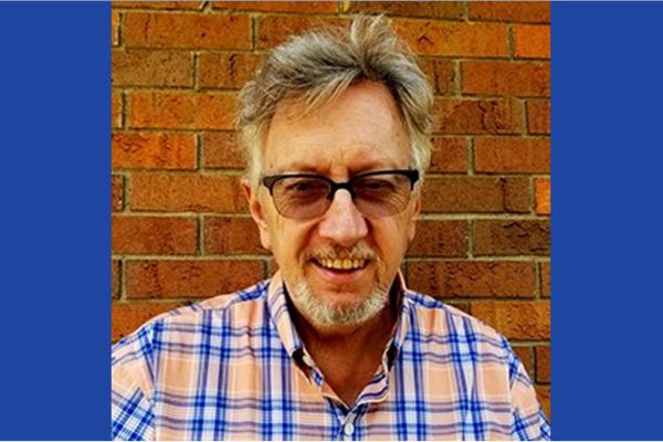 Dr. John Low wearing glasses, with a light orange and blue shirt.