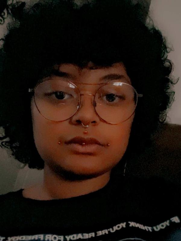 Individual in a black shirt and glasses, facing the camera head on with aviator styled glasses on.