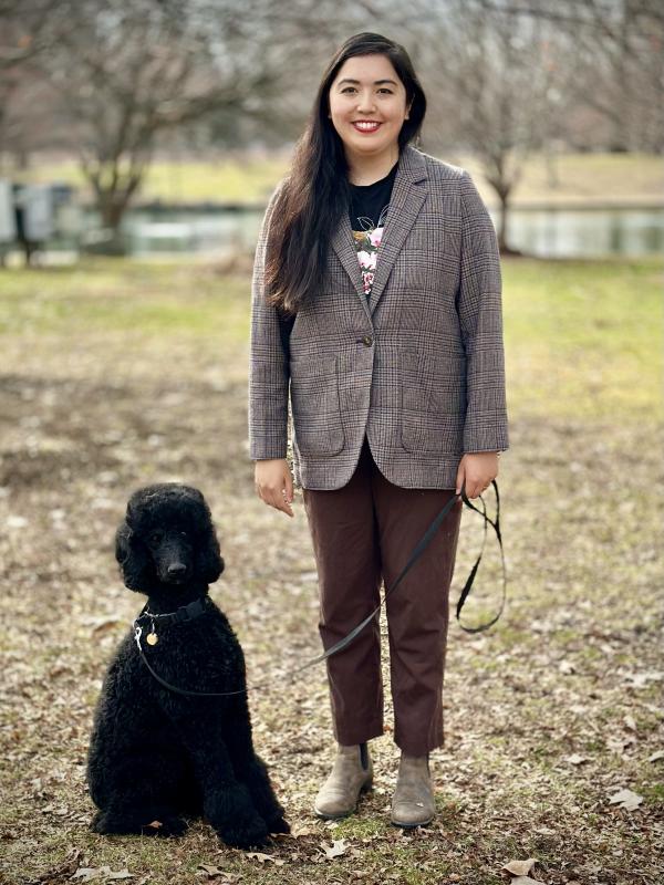Maya is standing, smiling next to her dog Rosalie who is a black standard poodle